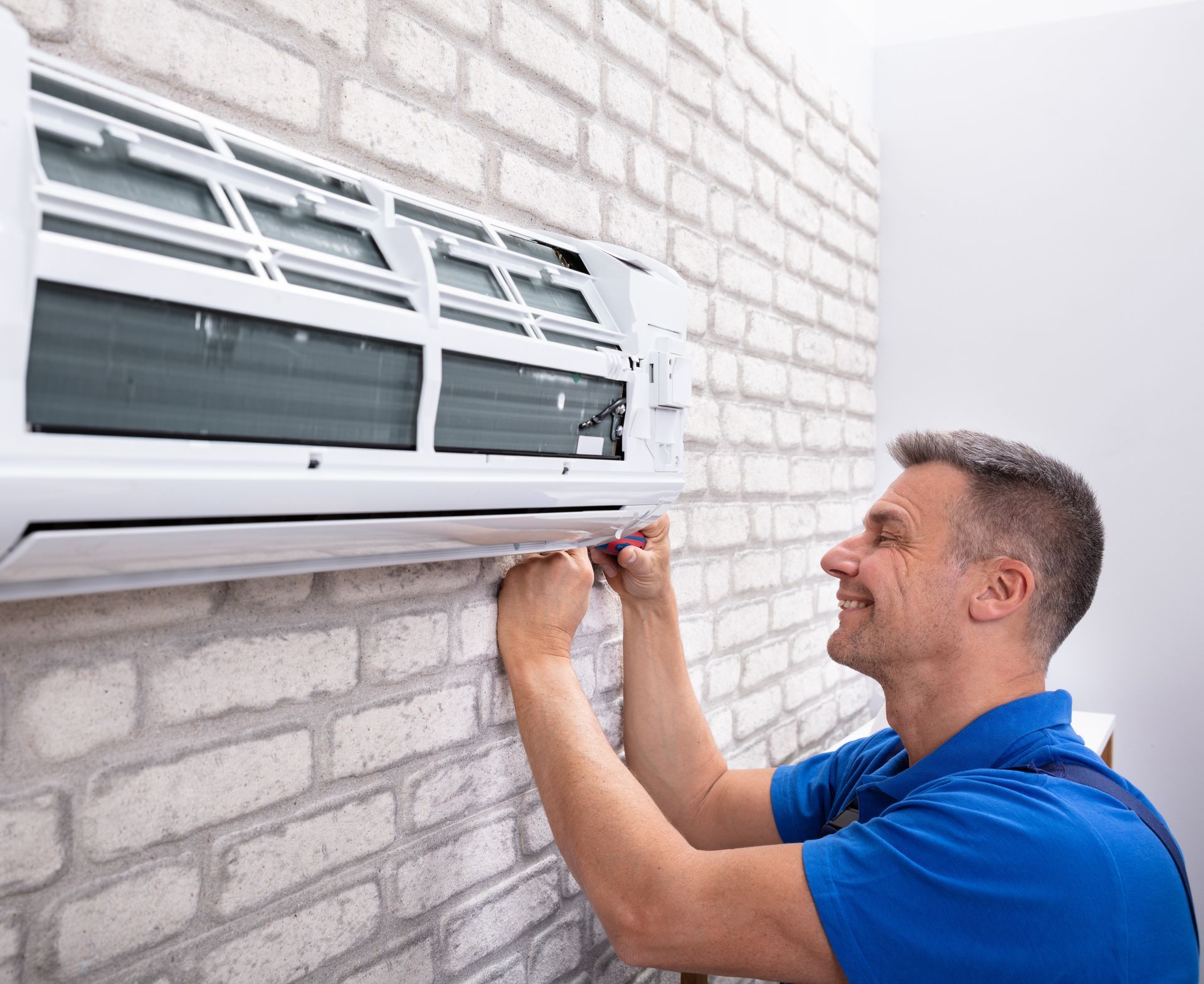 A technician is repairing a wall-mounted air conditioner unit using tools A technician is repairing a wall-mounted air conditioner unit using tools
