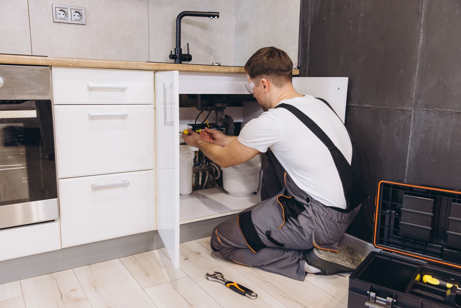 Plumber repairing pipes under kitchen sink with tools, installing plumbing system in home.