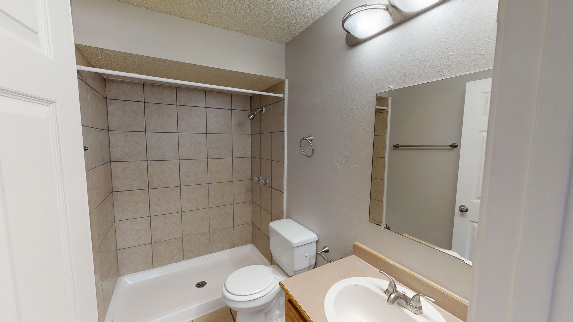 Small bathroom with a toilet, sink, mirror, and shower/tub with tiled walls.