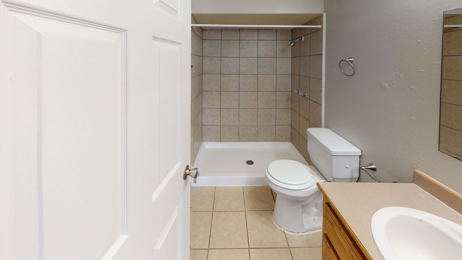 Bathroom with toilet, bathtub, sink, and beige tile floor, viewed through an open door