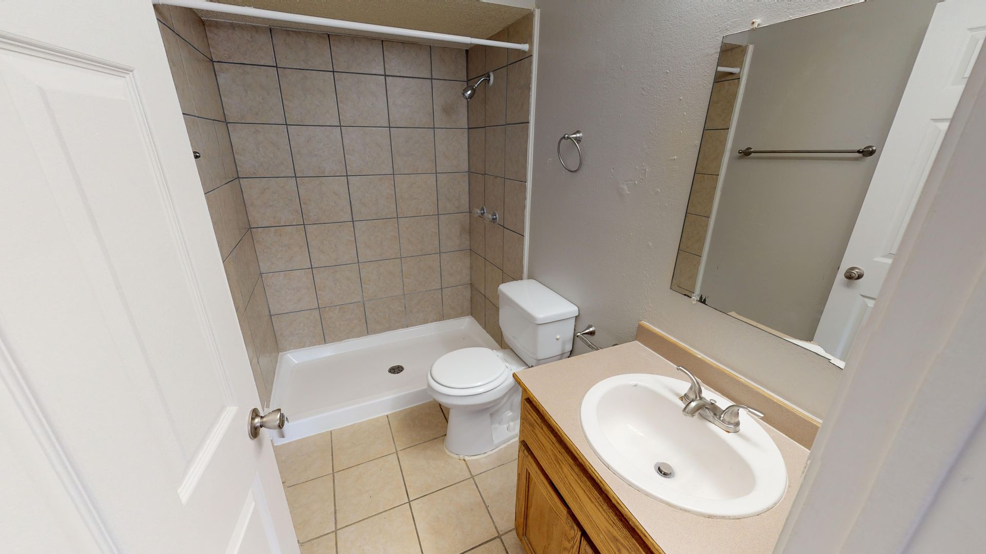 Small bathroom with a bathtub, toilet, sink, and mirror on beige tile floors and walls.