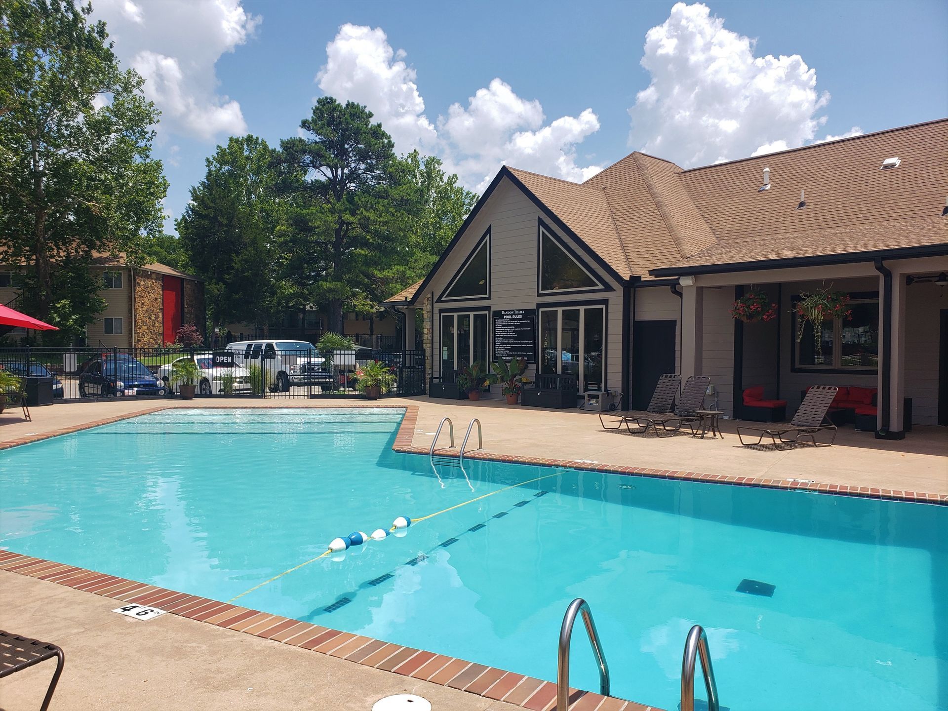 Outdoor swimming pool beside a tan house under a bright blue sky with fluffy clouds