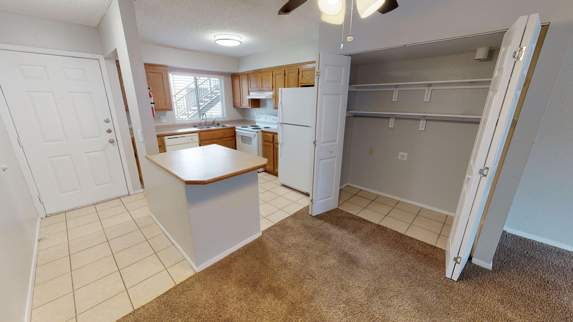 Empty kitchen with white cabinets, island, tiled floor, and open closet-style pantry in the foreground