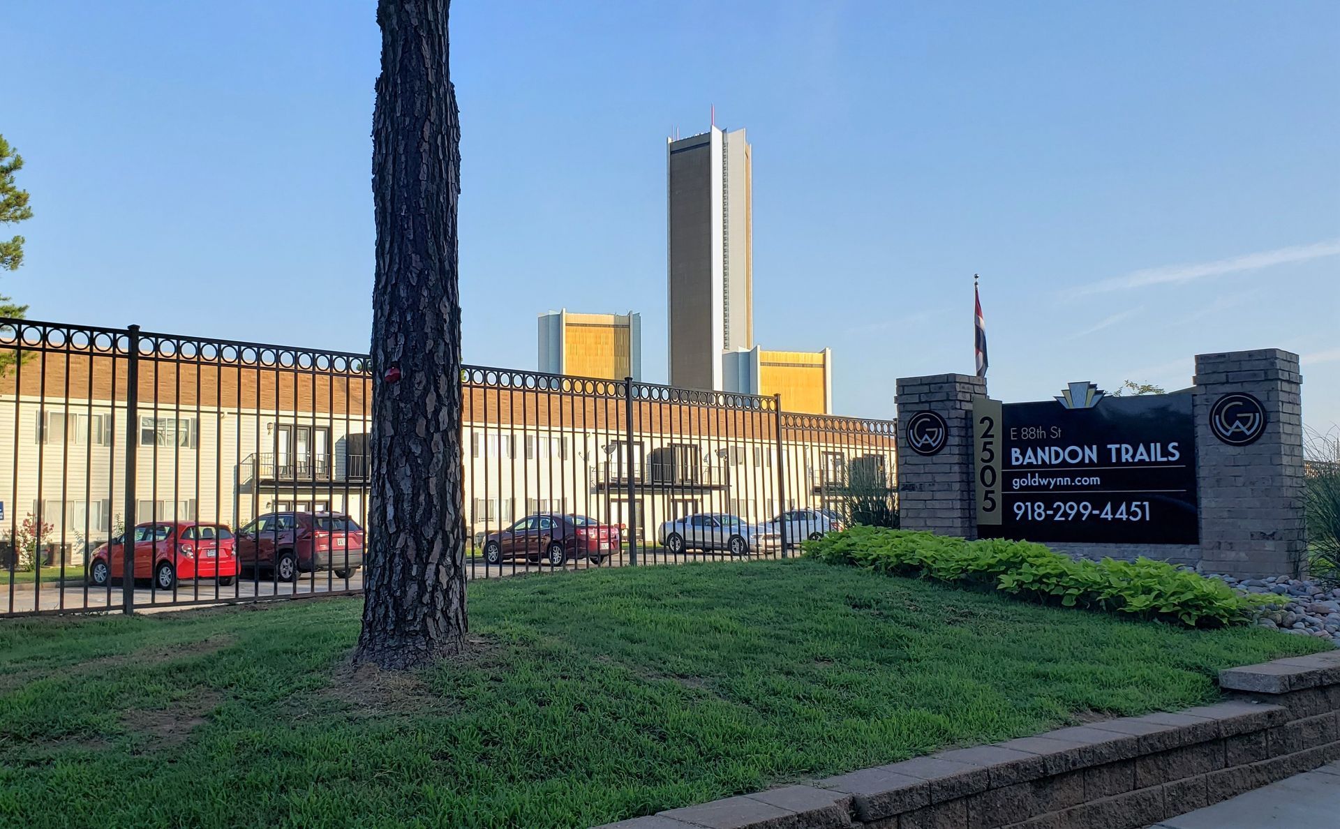 University building and sign beside a grassy lawn, with a tall tower in the background.