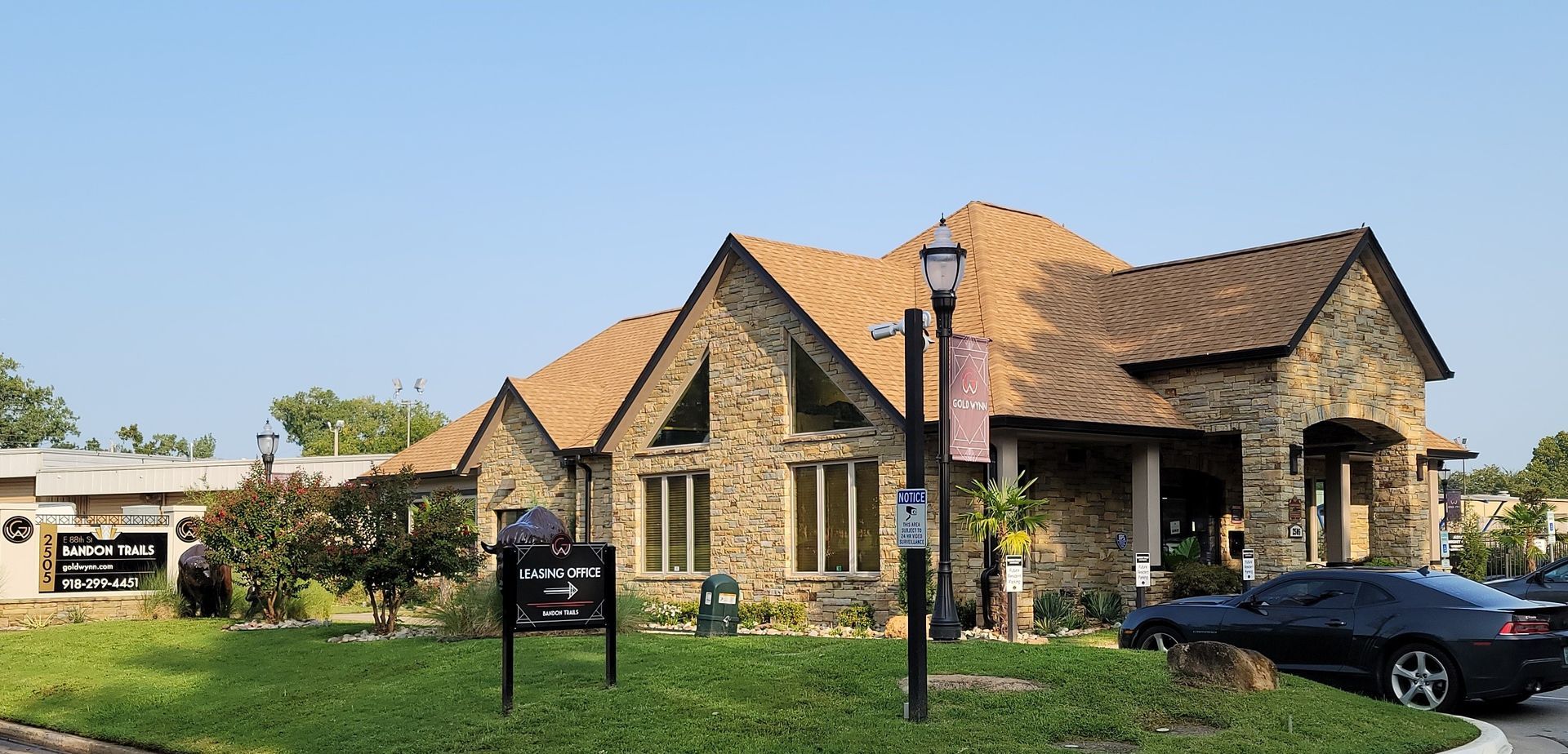 Stone house with a tiled roof and green lawn under a clear sky, parked car in the driveway