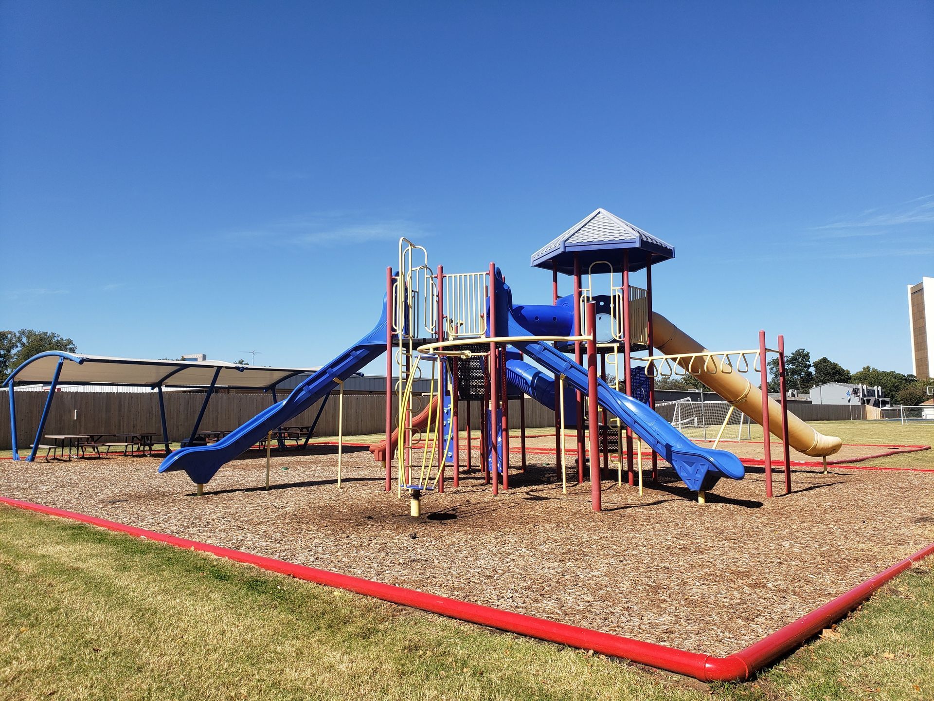 Playground with blue slides and climbing structures on a mulch surface under a clear sky.