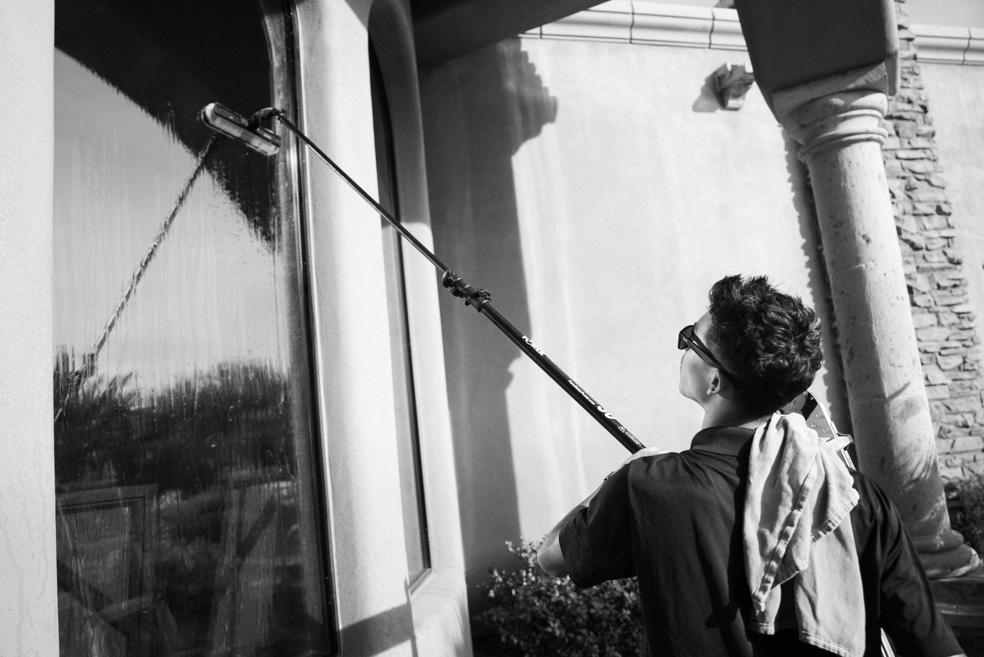 Person using a long pole to wash a large window beside a columned building