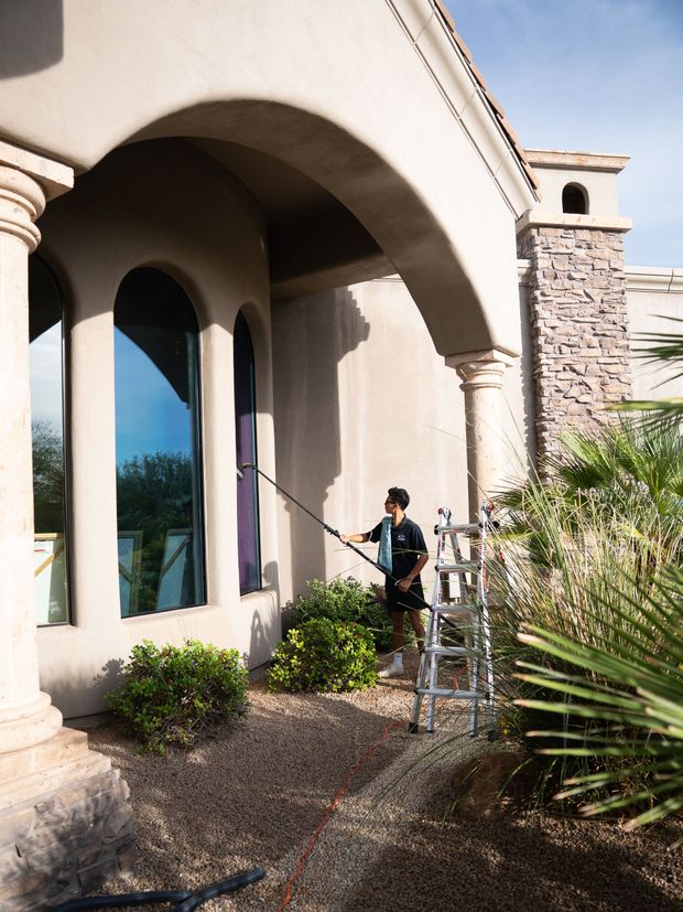 Person washing windows outside a beige stucco house with arched entry and stone columns