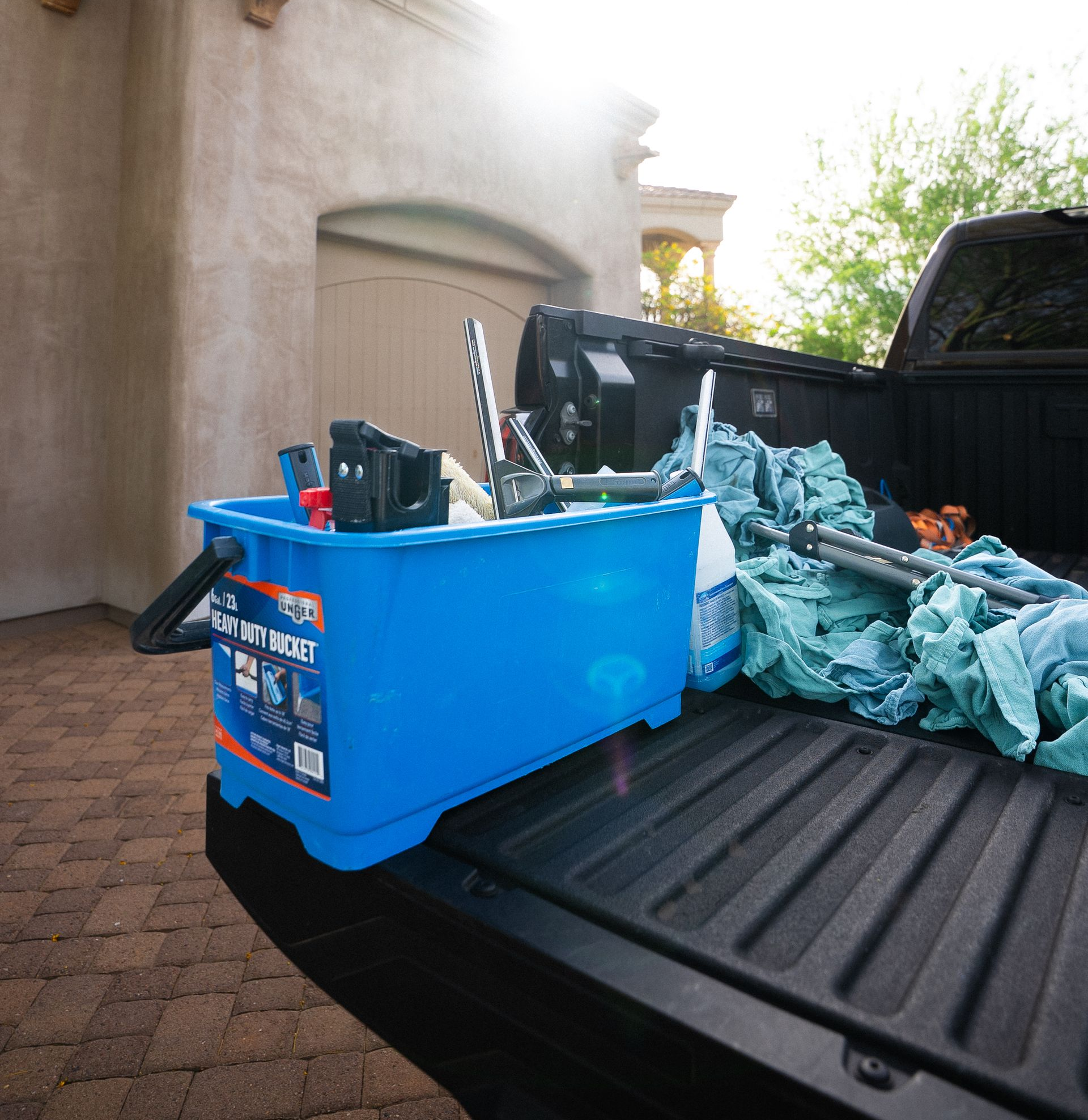 Blue dump bin and trash bags in the bed of a pickup truck by a garage driveway