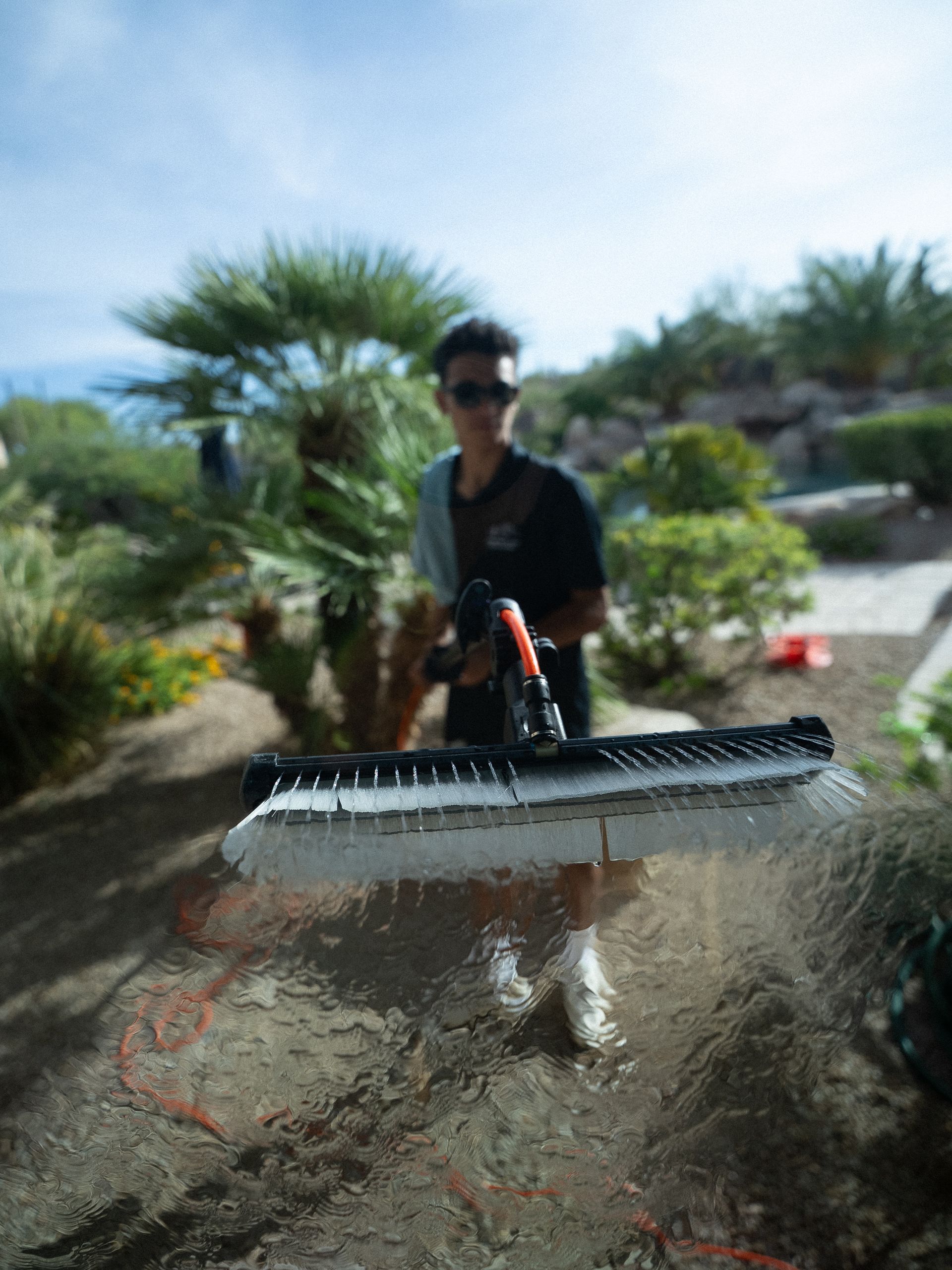 Person in sunglasses using a pressure washer outdoors on a sunny day
