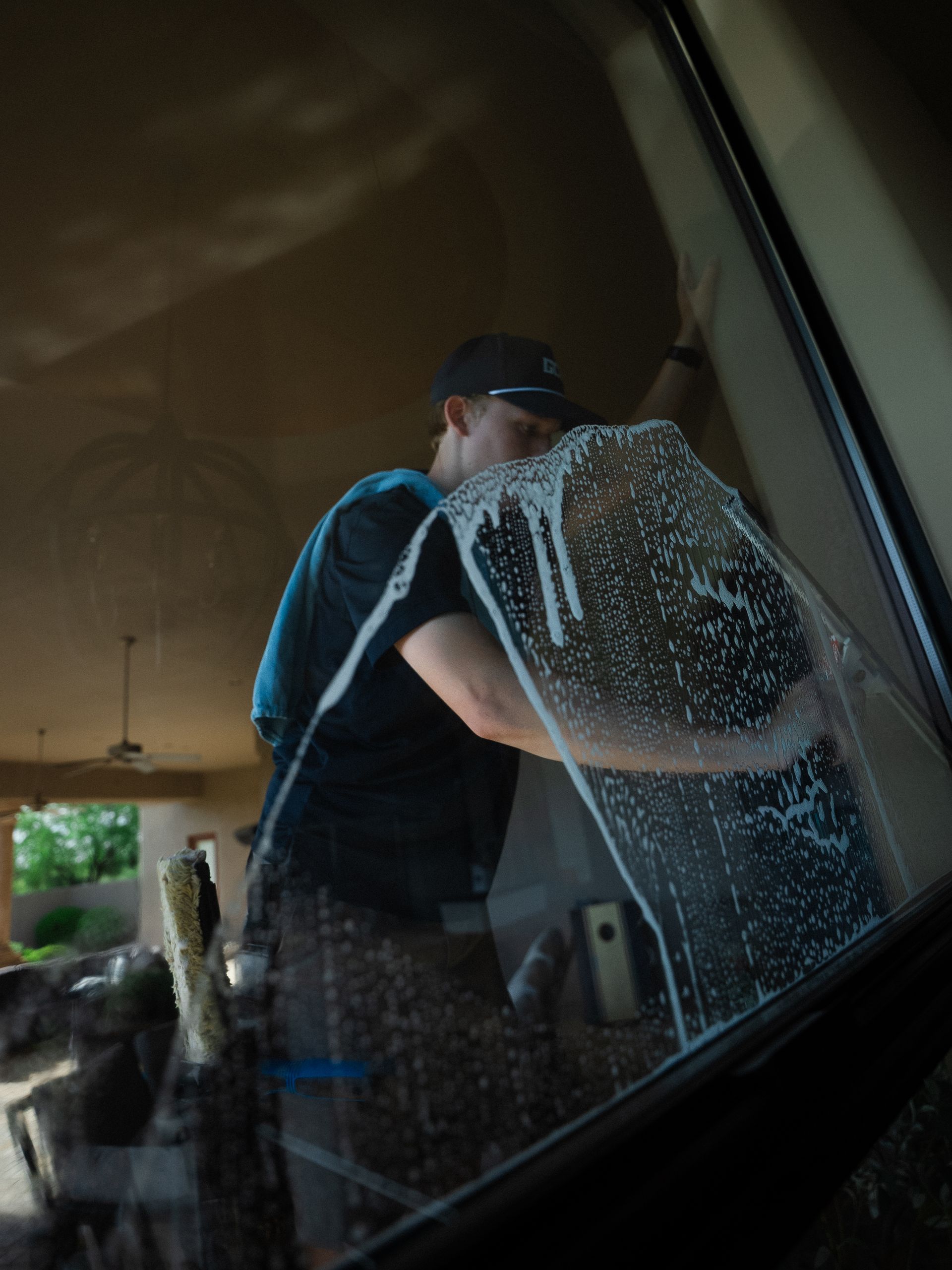 Person cleaning a large window with a squeegee, wearing a dark shirt and cap.