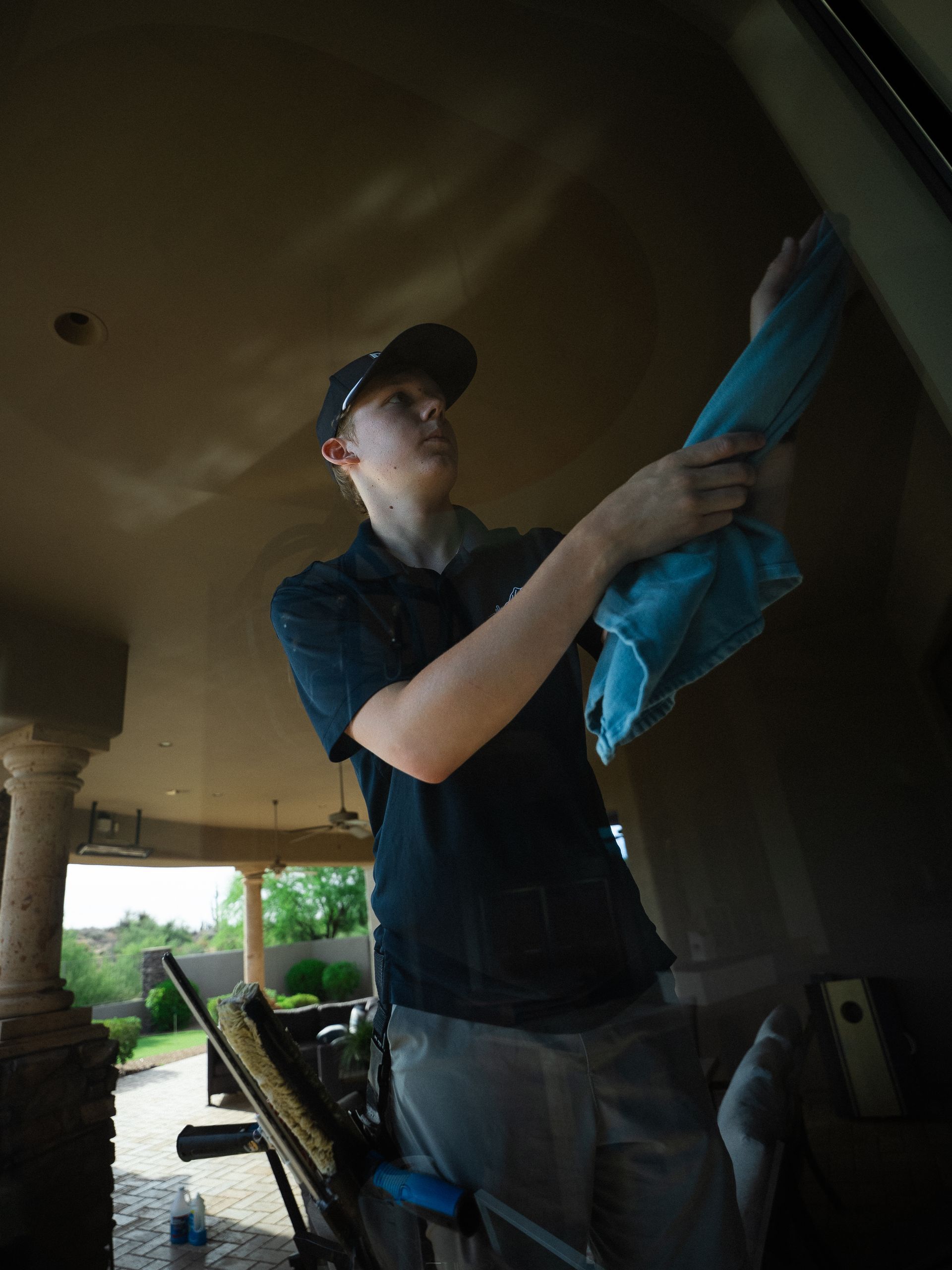 Person cleaning a ceiling with a blue cloth on a covered porch, holding a ladder nearby.