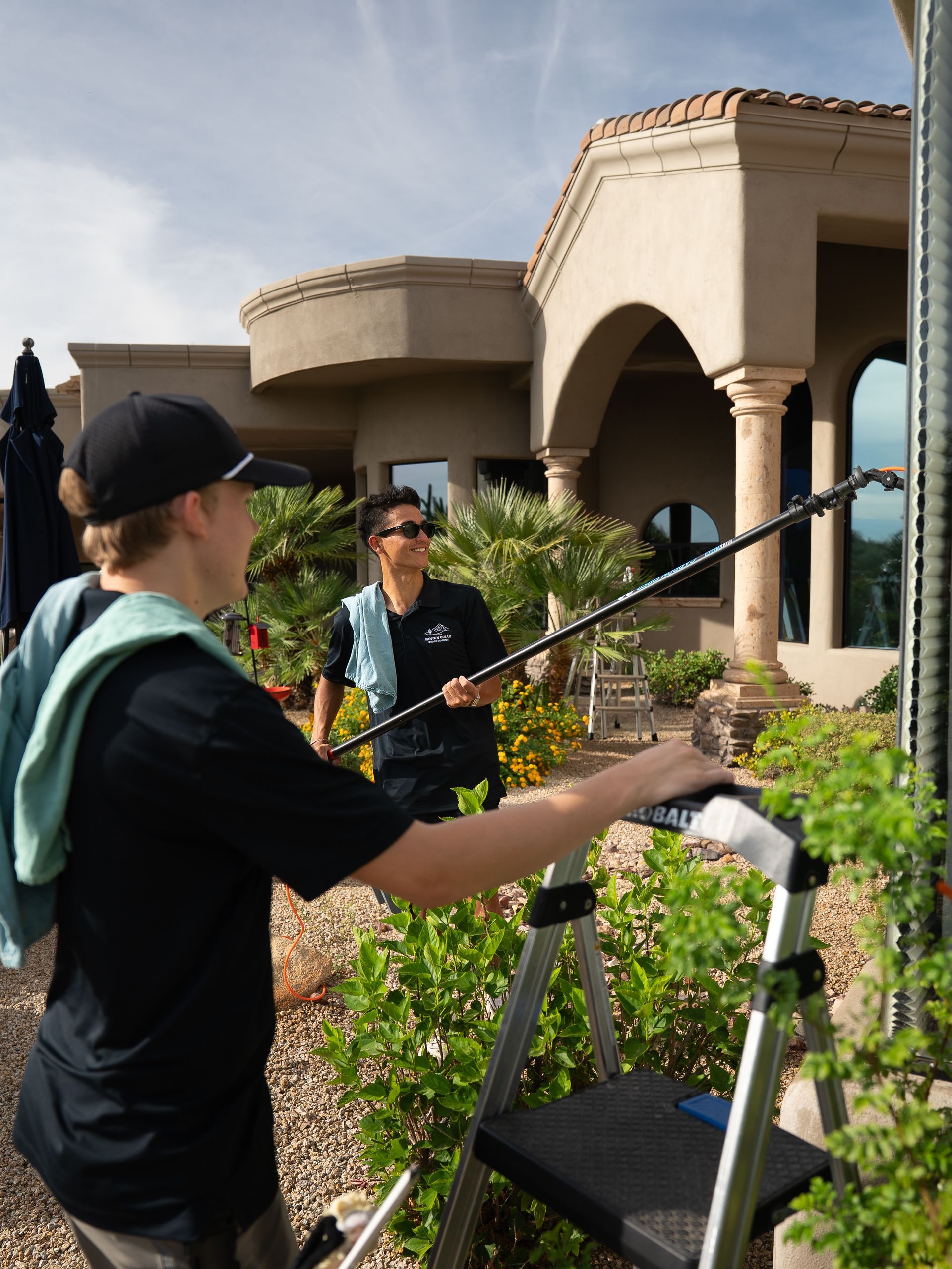 Two people setting up a camera tripod in a garden outside a stucco house