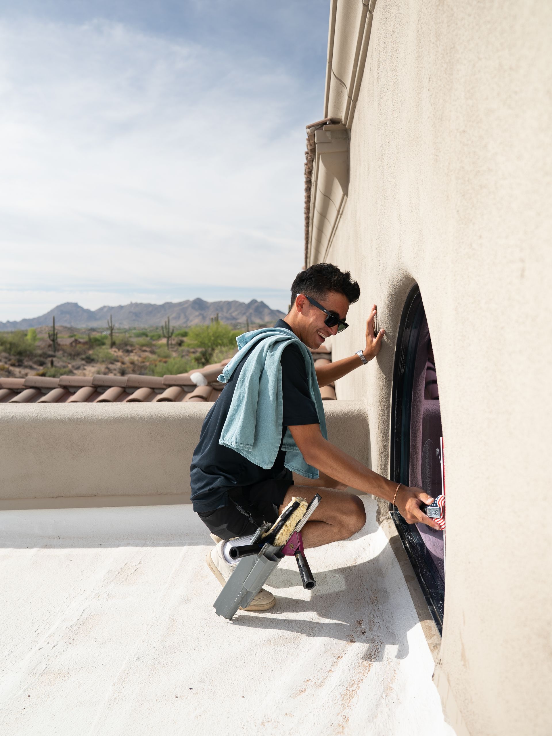 Person climbing through a small circular opening in a white wall on a rooftop, with mountains in the background