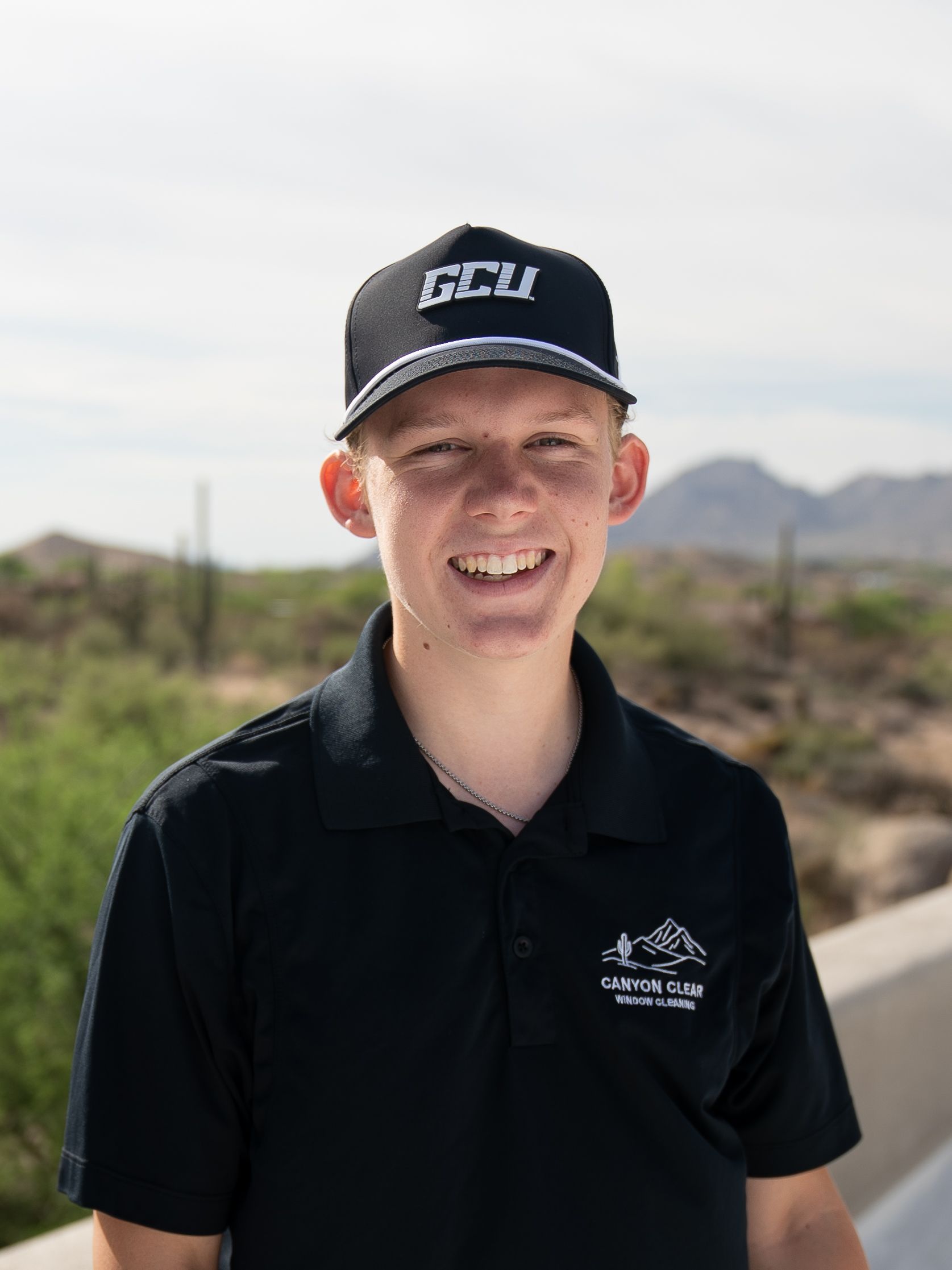 Person in black polo and cap smiling outdoors with mountains in the background