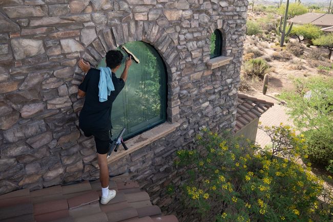 Person cleaning a stone house window with a squeegee on an outdoor staircase