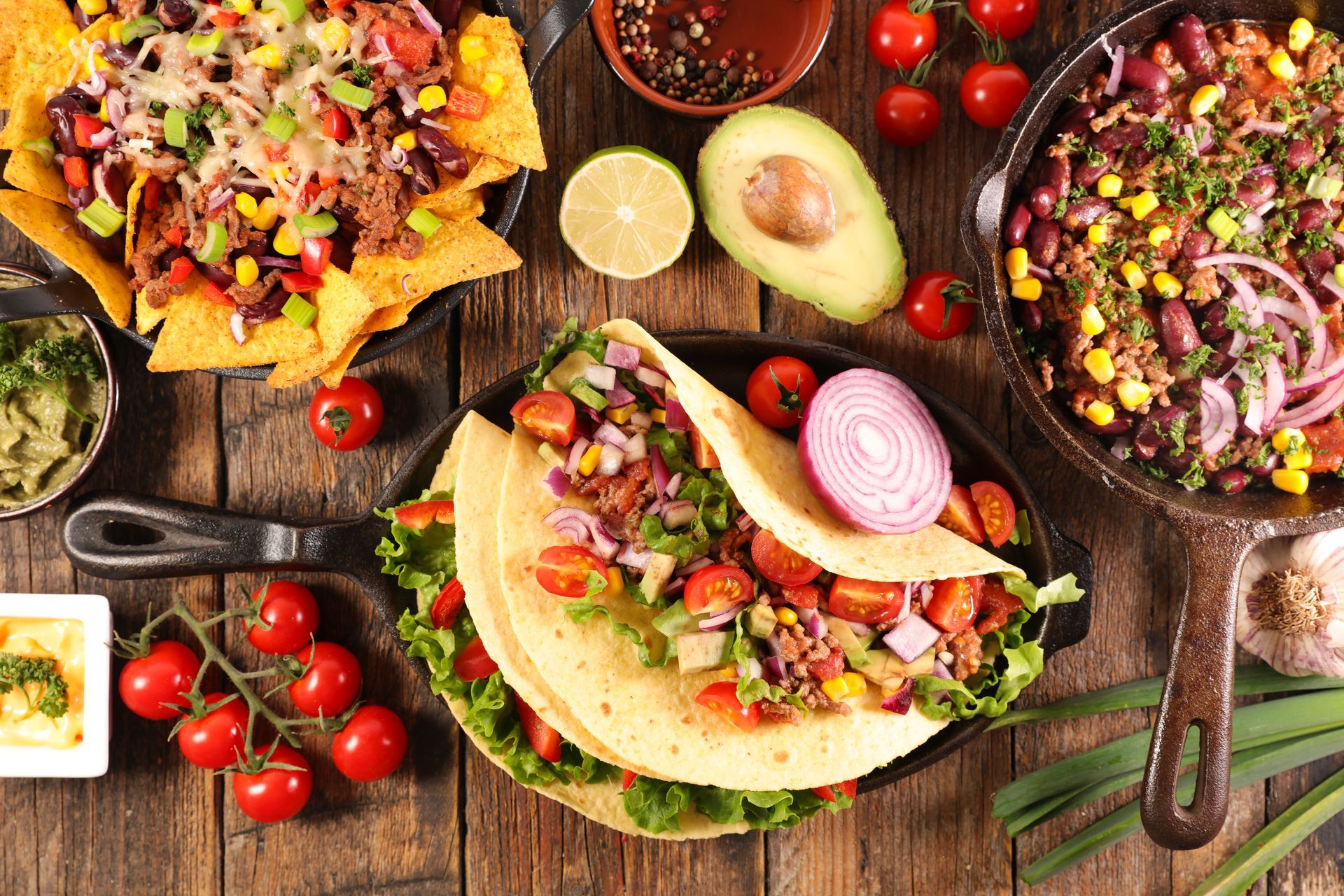 Three colorful tacos topped with vegetables on a rustic wooden table with avocados and salsa