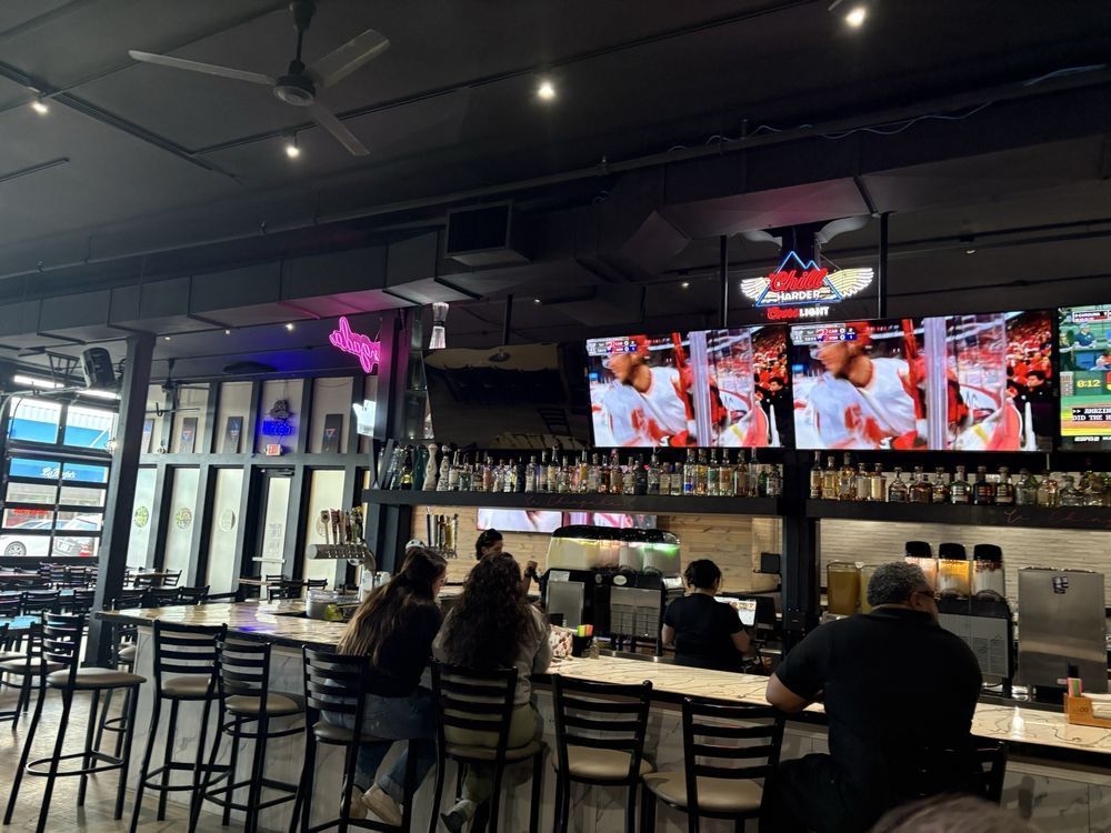 Modern sports bar with patrons seated at the counter beneath multiple TV screens and neon lighting