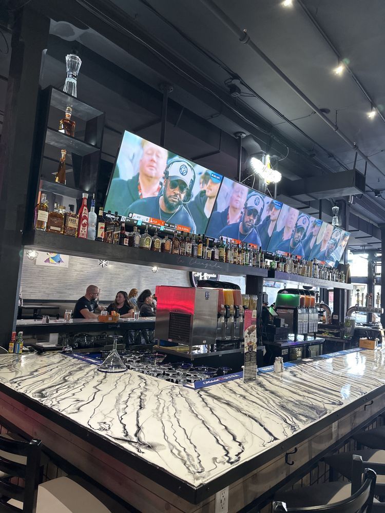 Bar with marble countertop, backlit liquor shelves, and multiple TV screens above the counter