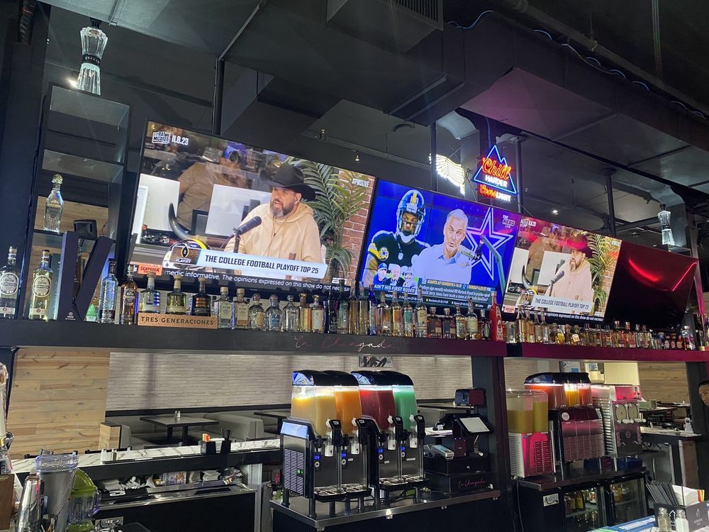 Bar with multiple TVs showing sports and news above a long row of liquor bottles and taps