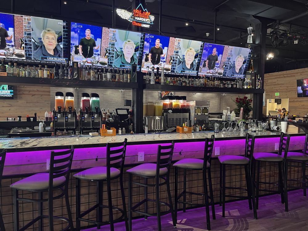 Empty modern bar with purple-lit counter, high stools, TVs, and beer taps behind the bar.
