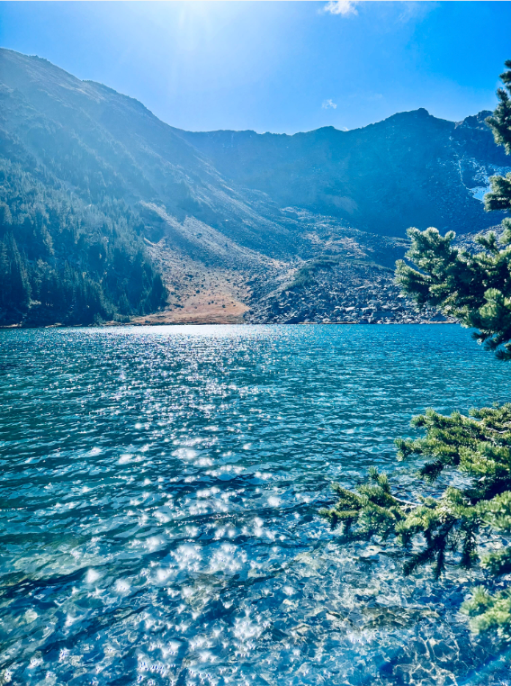 A lake surrounded by mountains and trees on a sunny day