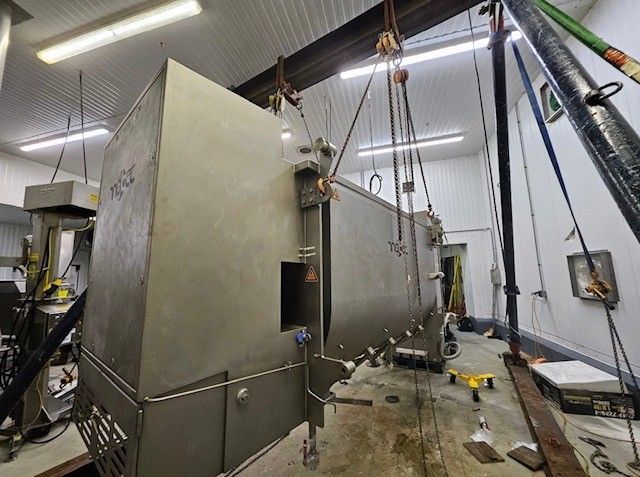 Large metal industrial equipment being lifted by a crane in a white warehouse.