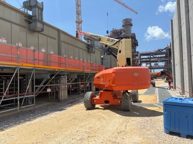 Orange construction lift at a power plant under construction. Scaffolding, crane, blue sky.