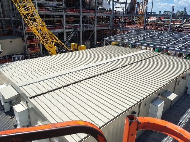 Overhead view of a large building with a metal roof, industrial setting, yellow crane in background.