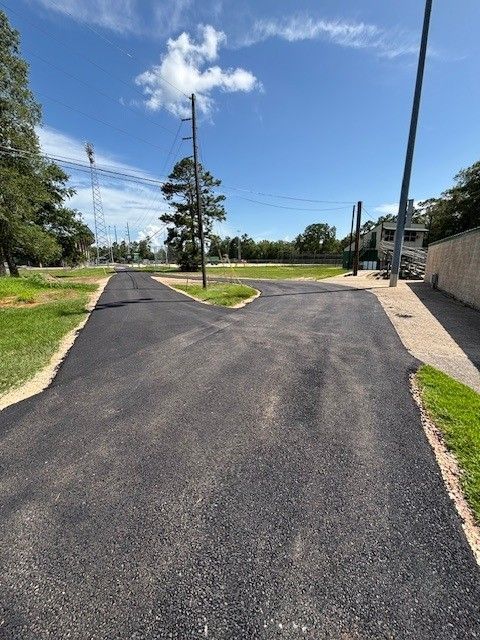 Newly paved asphalt road with a three-way intersection and power lines under a blue sky.
