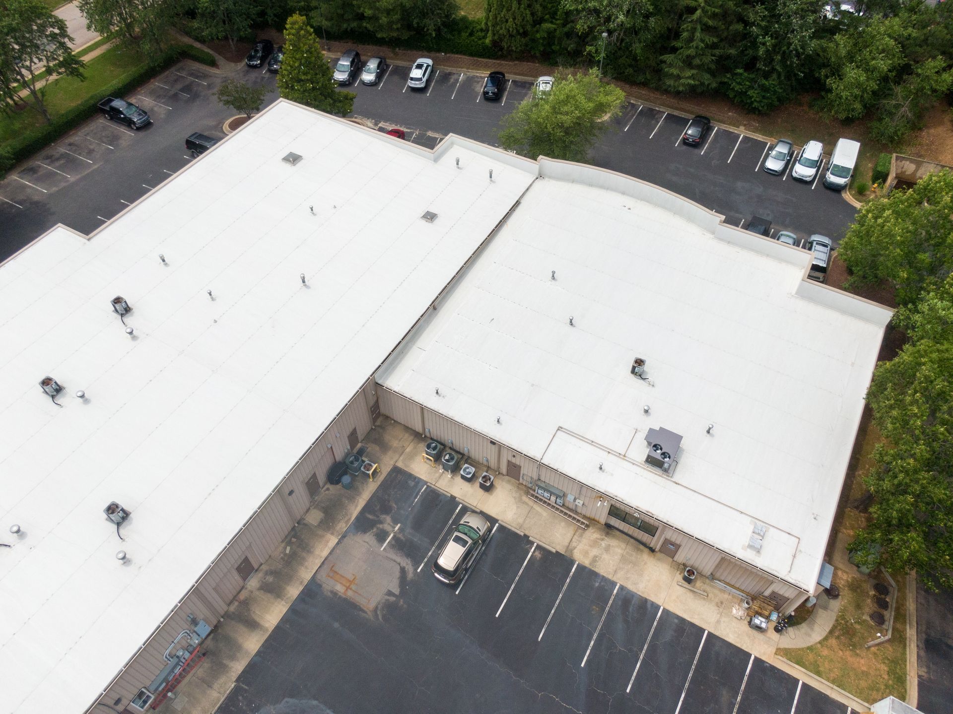 An aerial view of a building with a white roof and a parking lot.