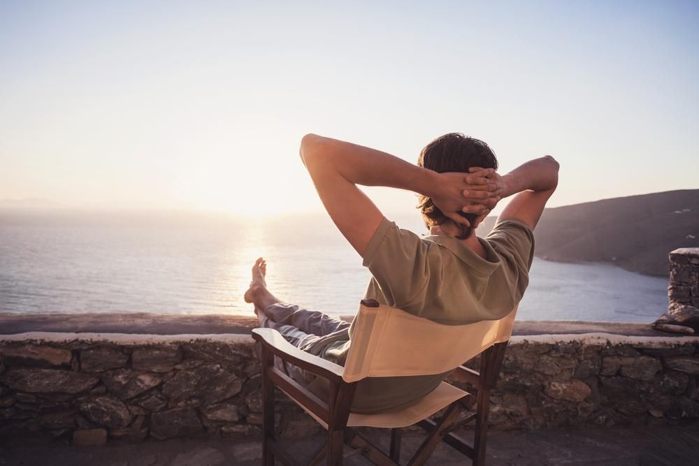 A Man Is Sitting In A Chair Overlooking The Ocean — Lake Macquarie Counselling & Psychotherapy In Newcastle, NSW
