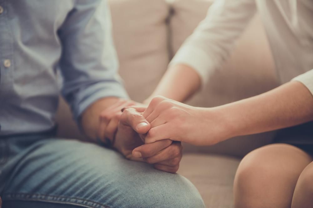 A Man And Woman Sit Together On A Couch, Holding Hands — Lake Macquarie Counselling & Psychotherapy In Cessnock, NSW