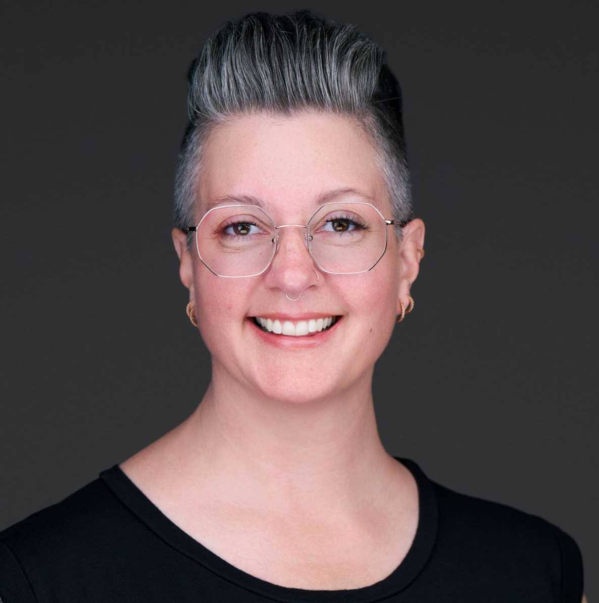 A woman wearing glasses and earrings is smiling for the camera.