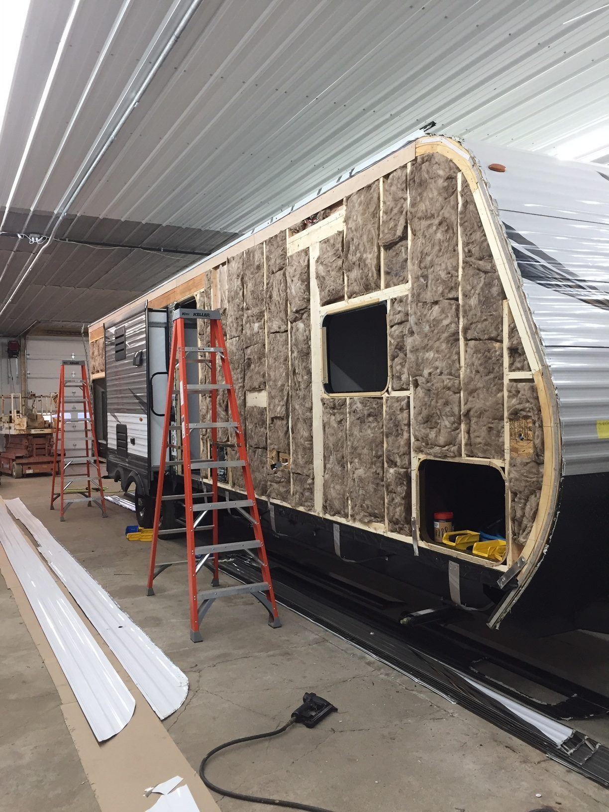 RV under construction with exposed insulation, wooden frame, ladders inside a workshop.