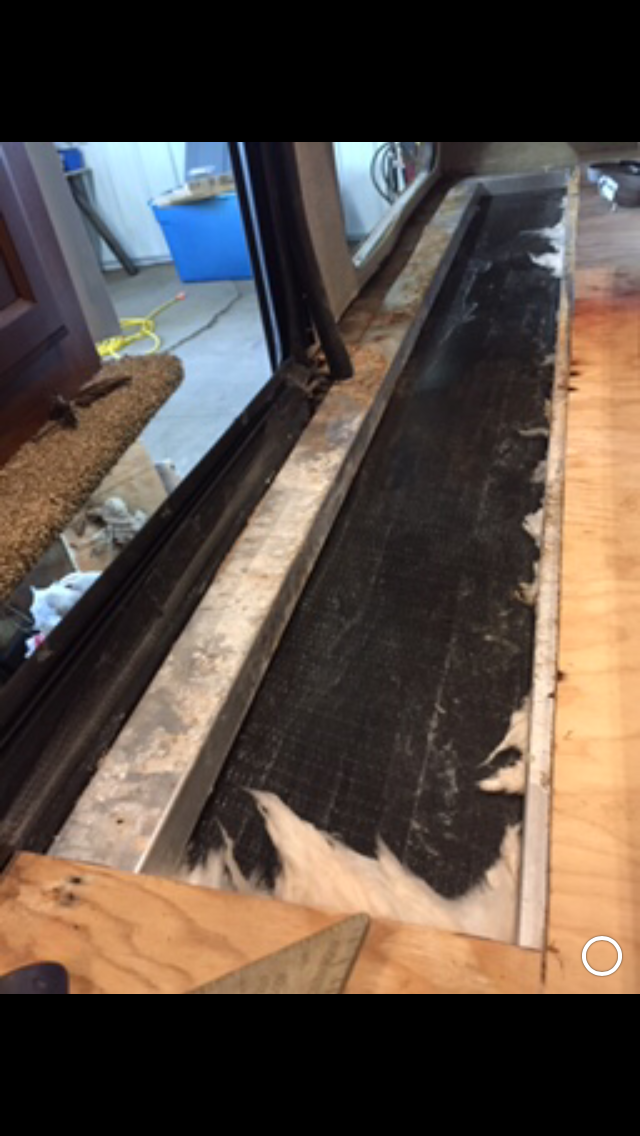 Wooden floor area with black, frayed material and metal framing.