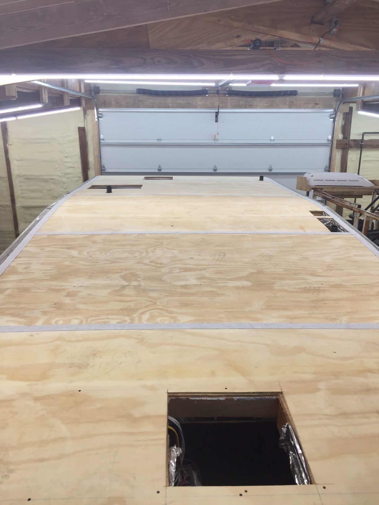 Overhead view of a wooden RV roof with a square opening and a garage door in the background.