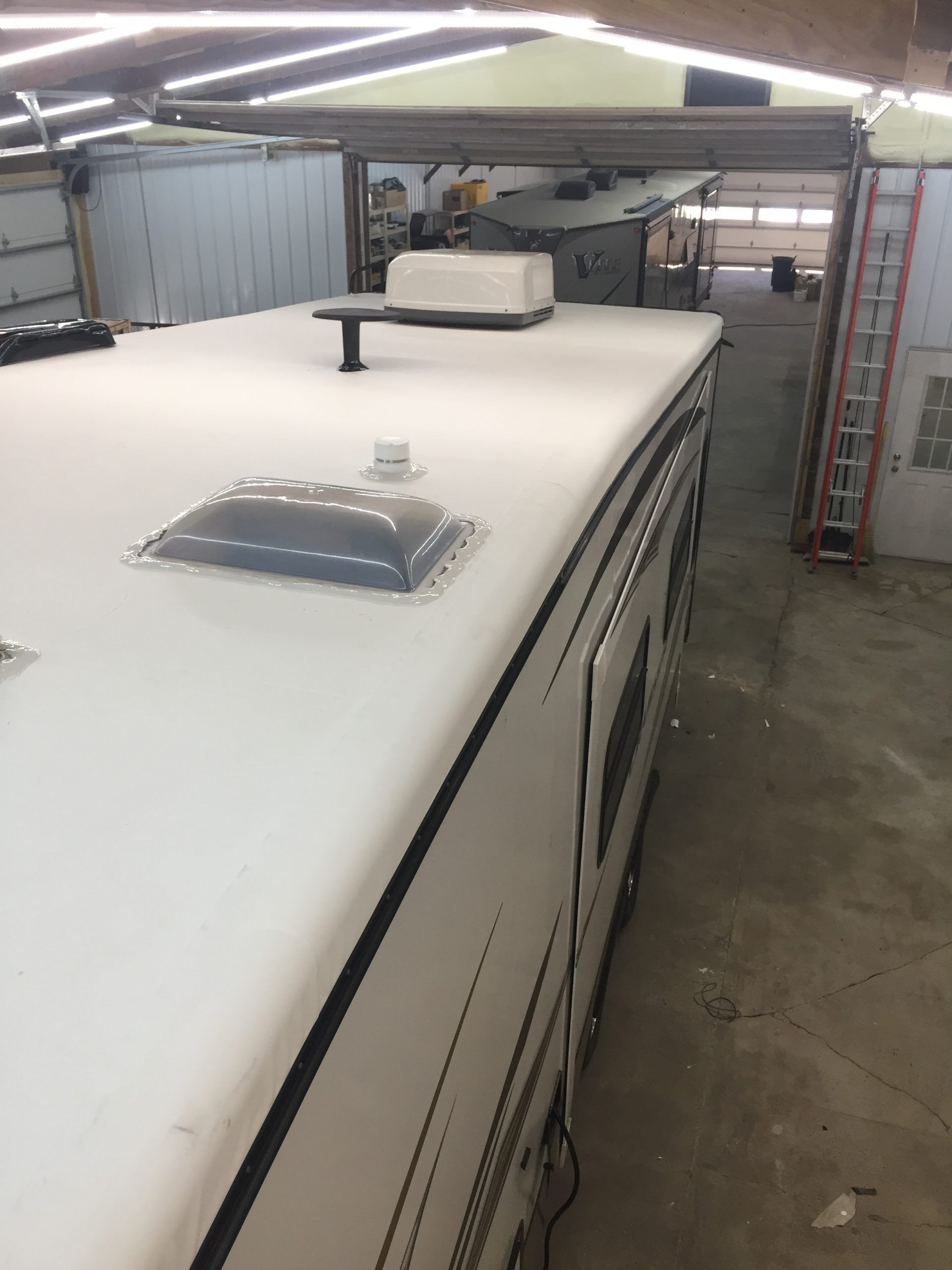 RV roof with vents and antenna under a metal roof in a garage.