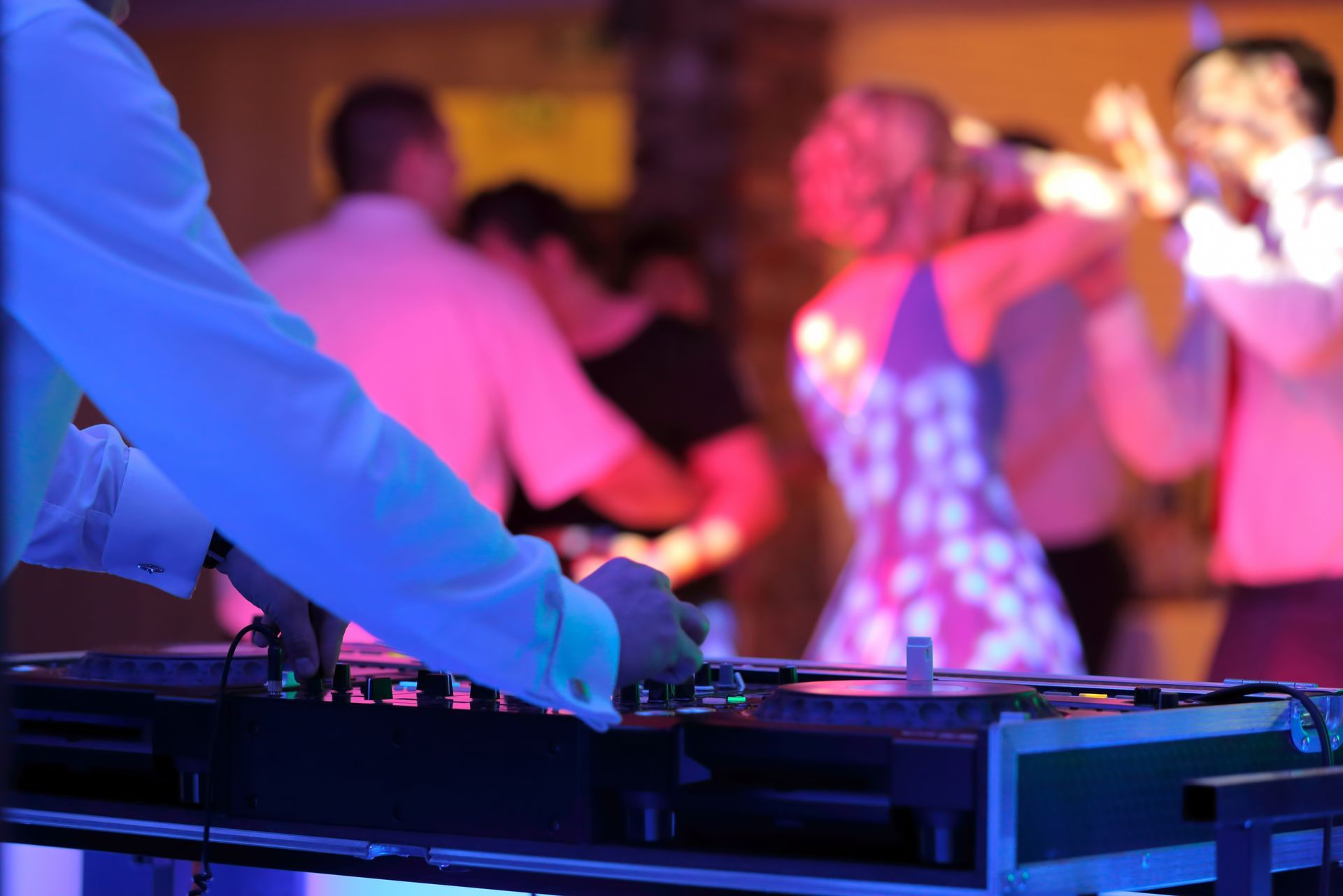 A dj is playing music at a party with people dancing in the background.