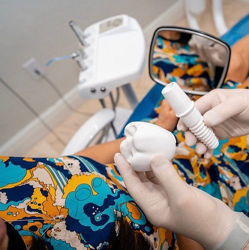 A woman is sitting in a dental chair holding a tooth and a mirror