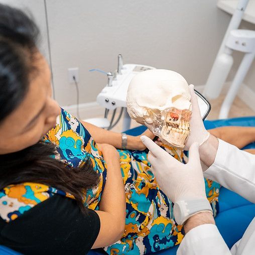 A woman is sitting in a dental chair while a dentist holds a model of a skull.