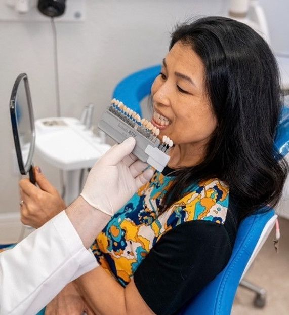 A woman is sitting in a dental chair looking at her teeth in a mirror