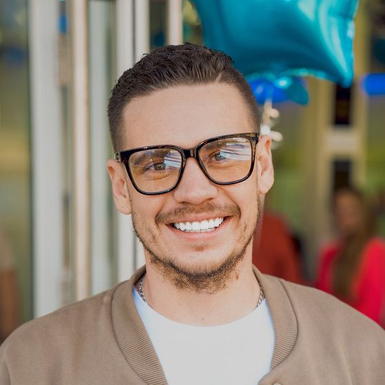 A man wearing glasses is smiling in front of a blue balloon.