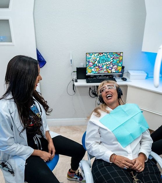 A woman in a dental chair is laughing while talking to a dentist