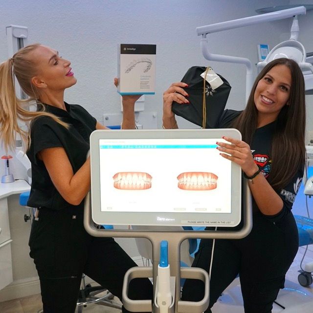 Two women in a dental office holding a box and a monitor with teeth on it