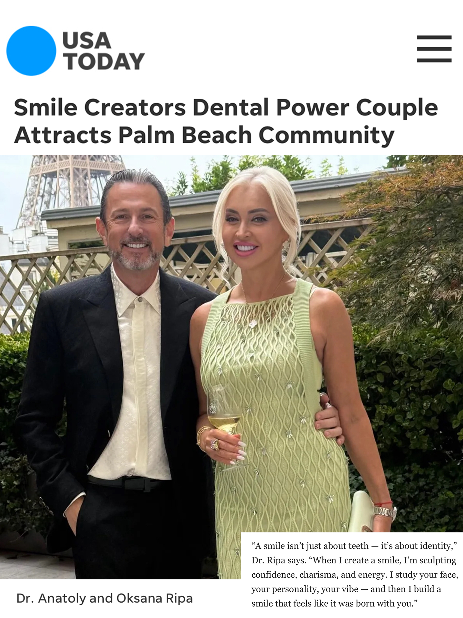 A man and woman smiling outdoors, posing for a photo. They are in front of foliage and a building.