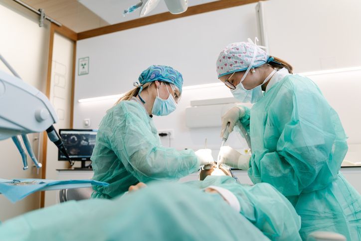Dentists in scrubs and masks performing a dental procedure on a patient in an office.