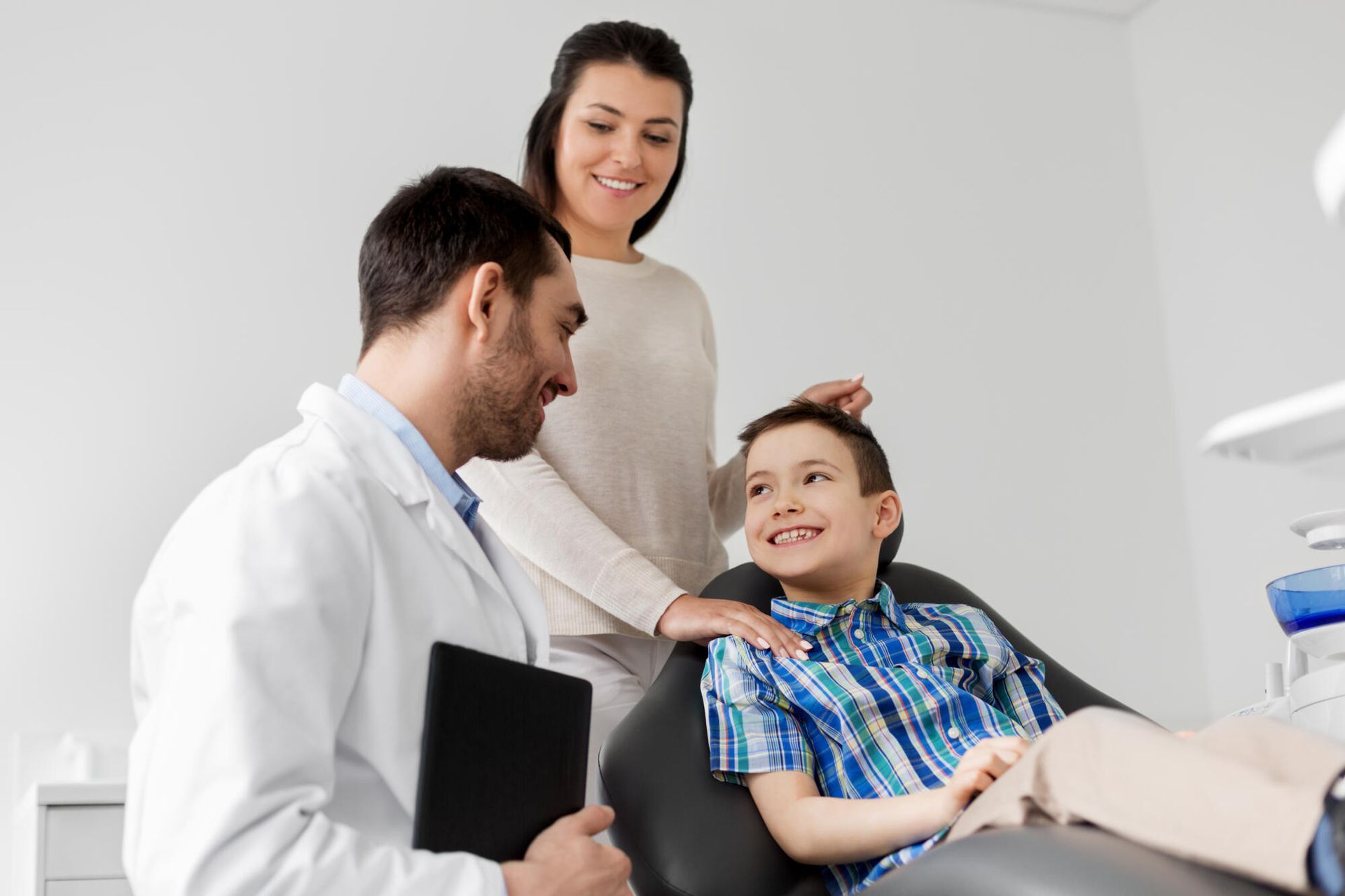 Doctor talking with a smiling child in a dental chair while a woman stands nearby