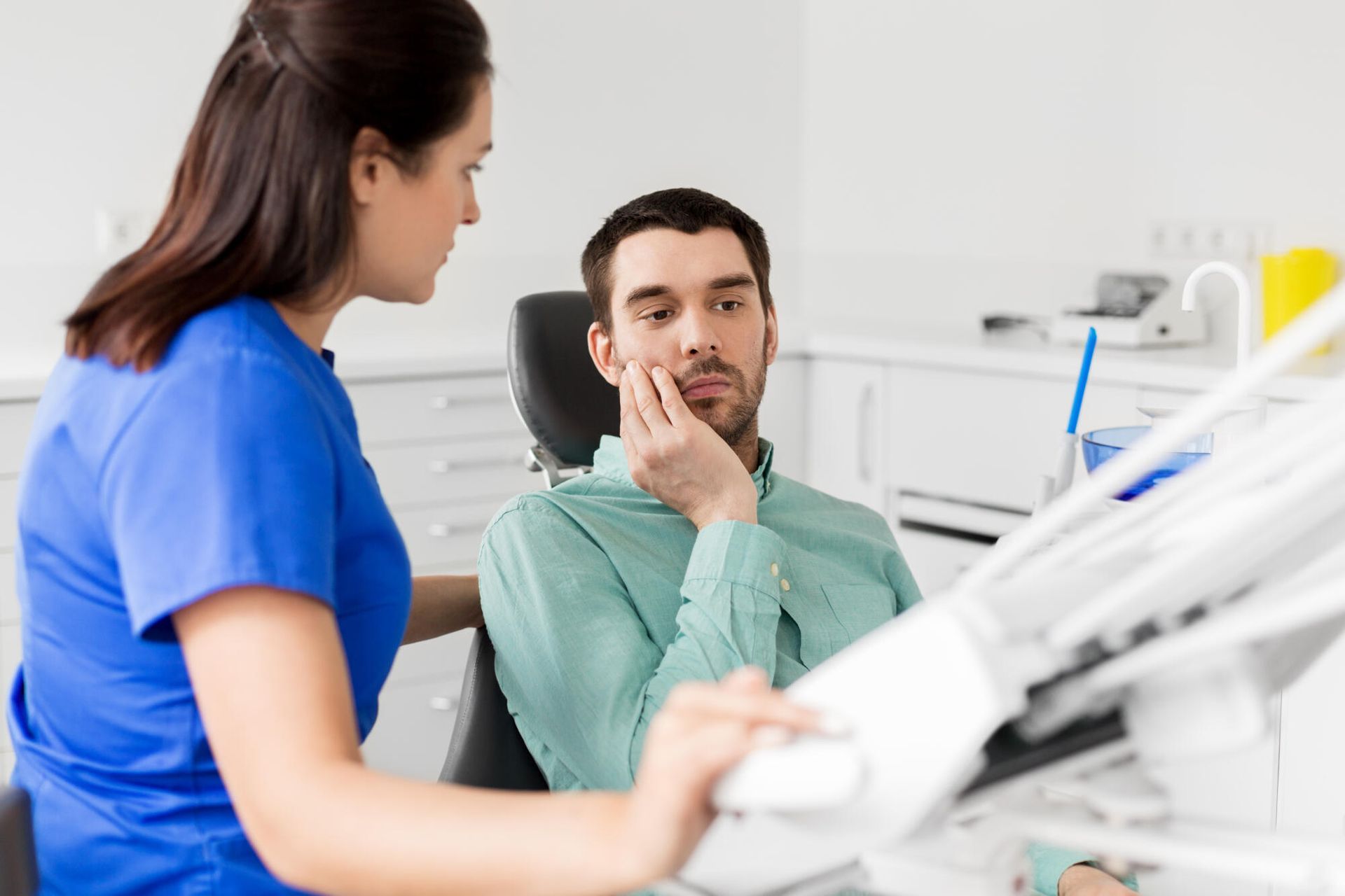 Dentist and patient discussing dental issue in a dental office. Patient appears concerned, holding his cheek.