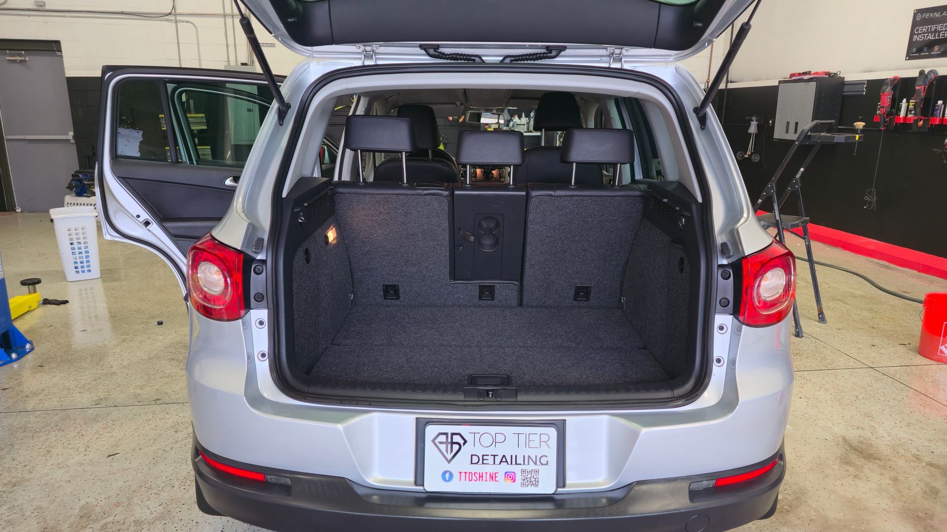 Silver SUV with trunk open, revealing cargo area and back seats in a detailing shop.